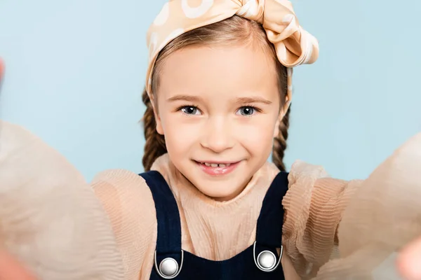 Fröhliches Kind mit Stirnband und Schleife, das isoliert auf blau in die Kamera blickt — Stockfoto