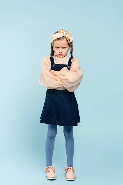 Full length of offended kid with pigtails standing with crossed arms on blue — Stock Photo