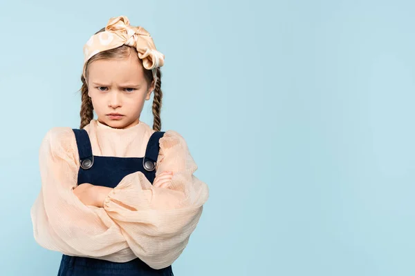 Offended kid with pigtails standing with crossed arms isolated on blue — Stock Photo