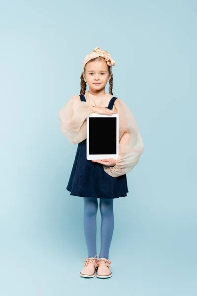 Volle Länge des kleinen Mädchens mit Zöpfen hält digitale Tablette mit leerem Bildschirm auf blau — Stockfoto