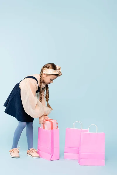Kleines Mädchen im Kleid legt Geschenk in Einkaufstasche auf blau — Stockfoto
