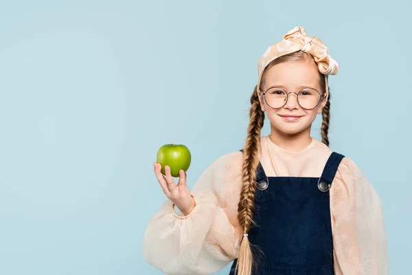 Smart kid dans des lunettes tenant pomme verte et souriant isolé sur bleu — Photo de stock