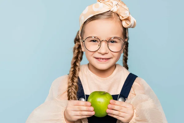 Glückliches Kind in Gläsern mit grünem Apfel und lächelt isoliert auf blauem Grund — Stockfoto