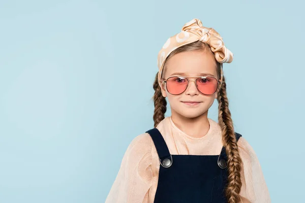 Маленька дівчинка в сонцезахисних окулярах дивиться на камеру ізольовано на синьому — стокове фото
