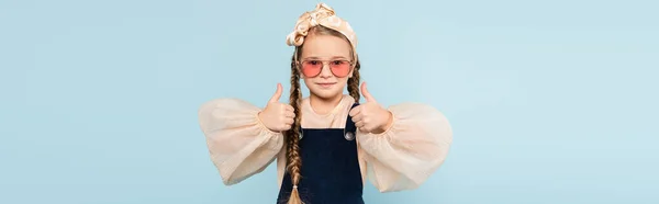 Petite fille en lunettes de soleil montrant pouces vers le haut isolé sur bleu, bannière — Photo de stock