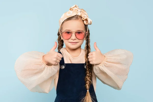 Little girl in sunglasses showing thumbs up isolated on blue — Stock Photo