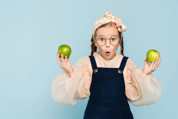 Enfant surpris dans des lunettes tenant des pommes vertes isolées sur bleu — Photo de stock