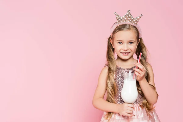 Felice bambina in abito e corona in possesso di vetro con frullato isolato su rosa — Foto stock