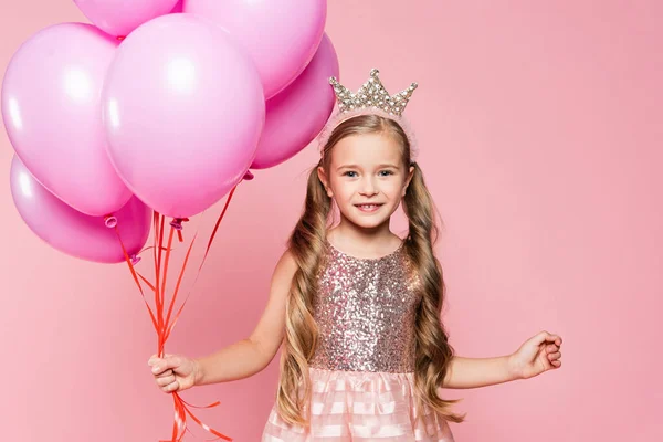 Menina alegre em vestido e coroa segurando balões isolados em rosa — Fotografia de Stock