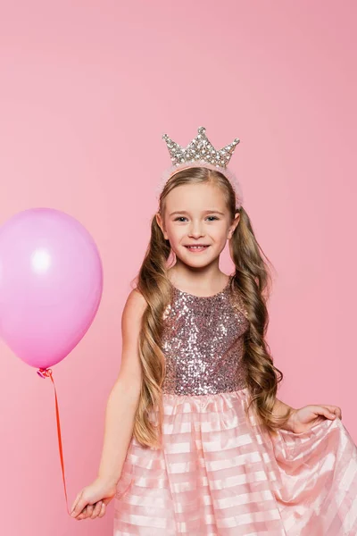 Menina alegre em vestido e coroa segurando balão isolado em rosa — Fotografia de Stock