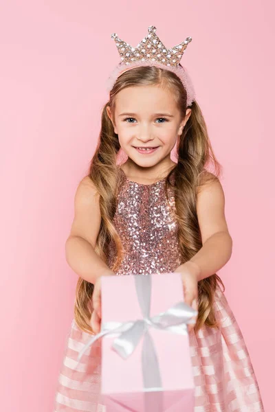 Щаслива маленька дівчинка в короні тримає загорнутий подарунок ізольовано на рожевому — стокове фото