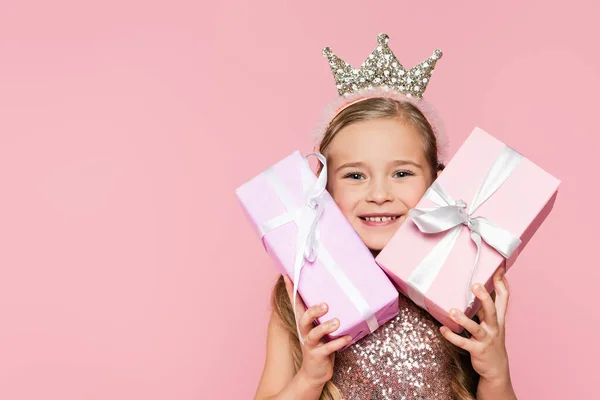 Happy little girl in crown holding wrapped presents isolated on pink — Stock Photo