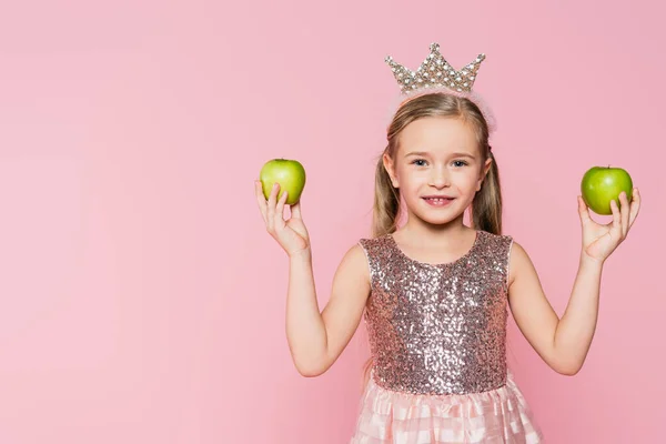 Щаслива маленька дівчинка в короні тримає зелені яблука ізольовані на рожевому — стокове фото