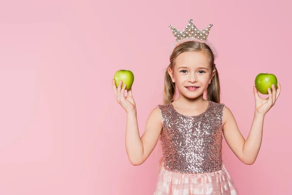 Happy little girl in crown holding green apples isolated on pink — Stock Photo