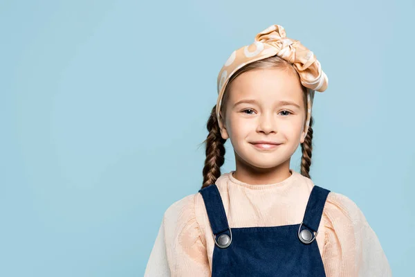 Fröhliches Kind mit Stirnband und Schleife, das isoliert auf blau in die Kamera blickt — Stockfoto