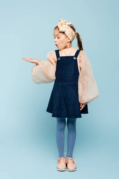 Полная длина удивленного ребенка в головном уборе с бантом, указывающим рукой на синий цвет — стоковое фото