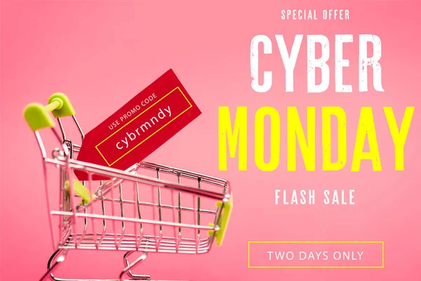 Red tag with use promo code cybr mndy lettering in small shopping trolley on pink — Stock Photo