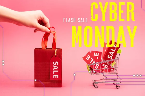 Ausgeschnittene Ansicht einer Frau mit kleiner Einkaufstasche in der Nähe des Warenkorbs mit Verkaufsetiketten in der Nähe von Cyber-Monday-Schriftzug auf rosa — Stockfoto