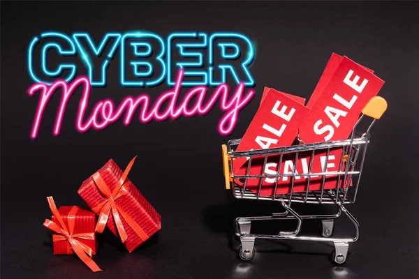 Red gifts near toy cart with sale tags near cyber monday lettering on dark background, black friday concept — Stock Photo