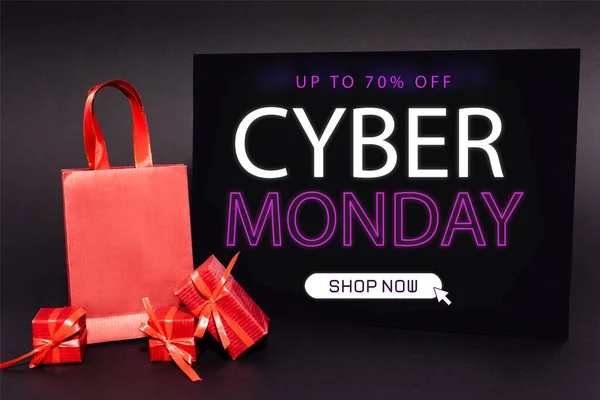 Red presents and shopping bag near placard with up to 70 percent off, cyber monday, shop now lettering on dark background — Stock Photo