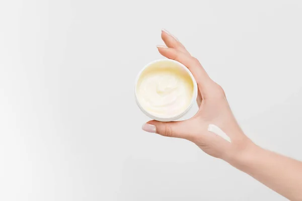 Vue partielle de la femme tenant récipient avec crème cosmétique à la main isolé sur blanc — Photo de stock