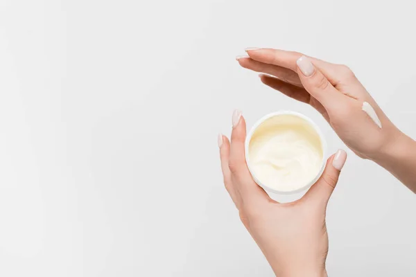 Vista parcial de la mujer sosteniendo contenedor con crema cosmética aislado en blanco - foto de stock