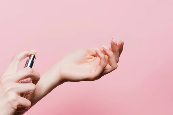 Vista parcial de la mujer sosteniendo la botella y aplicando perfume de lujo aislado en rosa - foto de stock