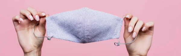 Vista ritagliata della donna che tiene maschera protettiva in cotone in mani isolate su rosa, banner — Foto stock