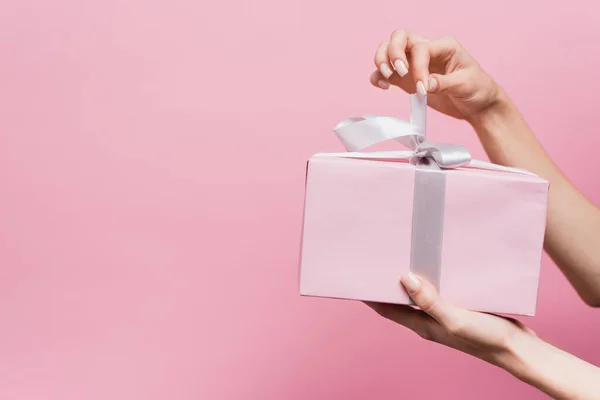 Vista parcial de la mujer sosteniendo cinta en regalo envuelto aislado en rosa - foto de stock