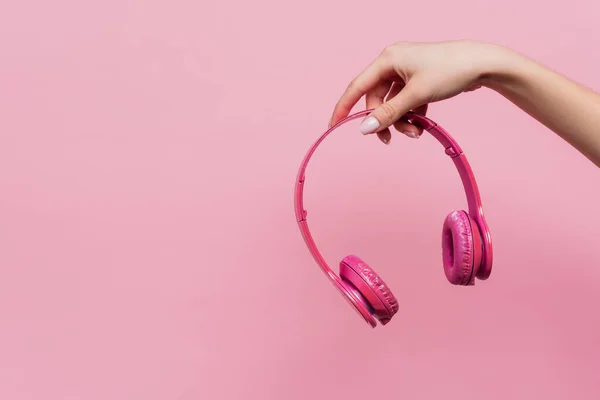 Vista parcial de la mujer sosteniendo auriculares inalámbricos en la mano aislados en rosa - foto de stock