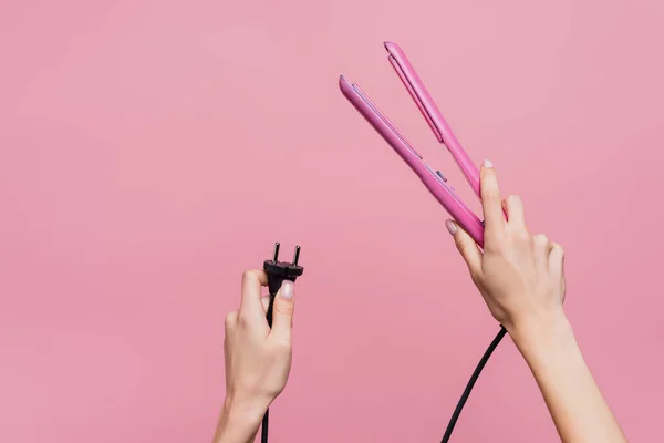 Cropped view of woman holding hair straightener in hands isolated on pink — Stock Photo
