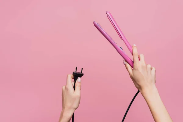 Vista recortada de la mujer sosteniendo plancha de pelo en las manos aisladas en rosa - foto de stock