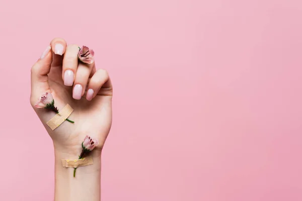 Plasters with flowers on female hand isolated on pink — Stock Photo