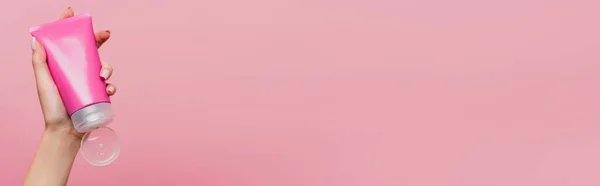 Vue partielle de la femme tenant tube avec lotion à la main isolé sur rose, bannière — Photo de stock