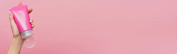 Visión parcial de la mujer que sostiene el tubo con la loción en la mano aislada en rosa, bandera - foto de stock