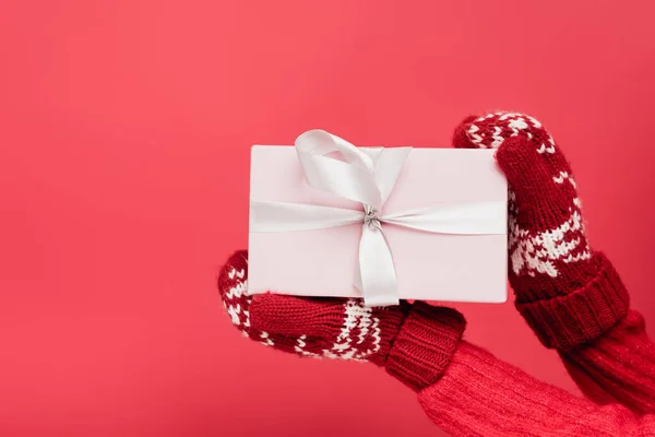 Cropped view of woman in mittens holding wrapped present isolated on red — Stock Photo