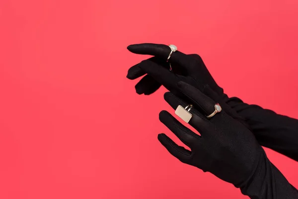 Vista recortada de las manos femeninas en guantes negros con anillos dorados aislados en rojo - foto de stock