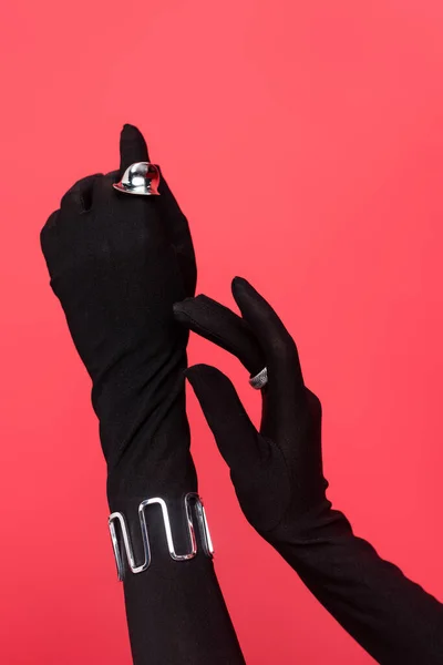 Corte das mãos femininas em luvas pretas com anéis e pulseira isolada em vermelho — Fotografia de Stock