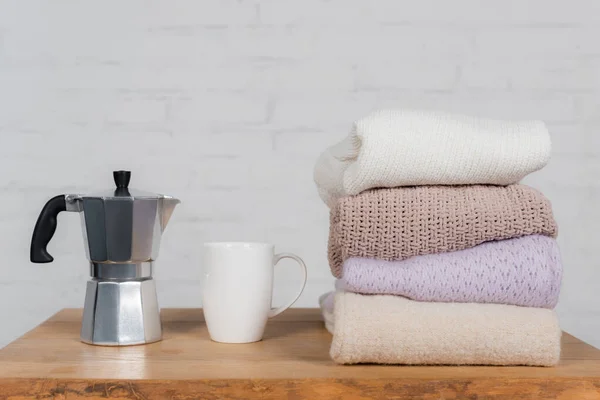 Cafetera, taza y suéteres de lana sobre mesa de madera - foto de stock