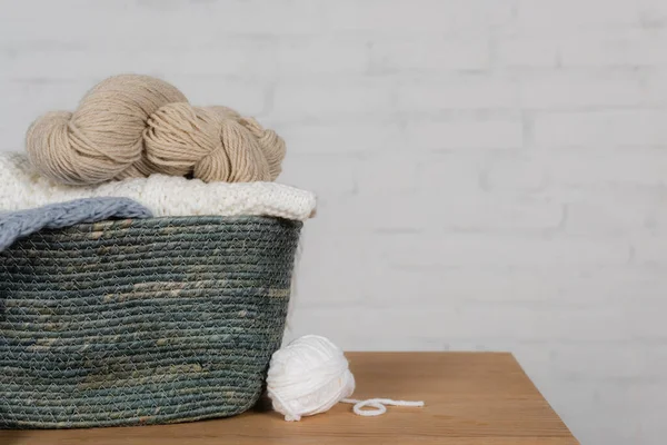 Basket with woolen yarns on wooden table near white brick wall — Stock Photo