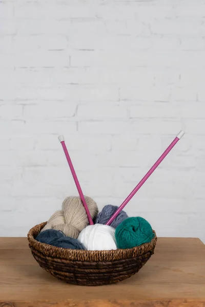 Needless in basket with yarn balls on wooden table and brick wall at background — Stock Photo