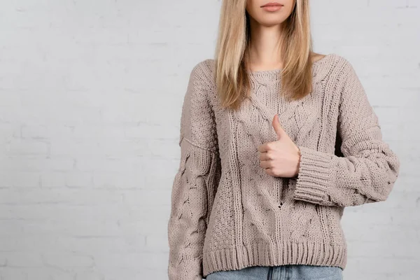 Vista recortada de la mujer joven en suéter de punto que muestra como sobre fondo blanco - foto de stock