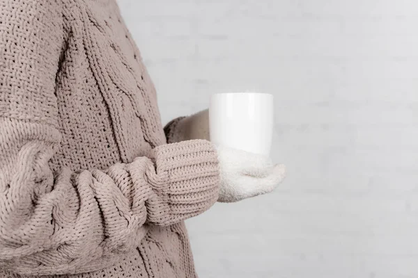 Vue recadrée de la femme en pull chaud et gants tenant tasse sur fond blanc — Photo de stock