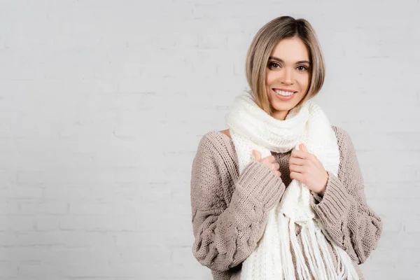 Donna sorridente in maglia maglione e sciarpa guardando la fotocamera su sfondo bianco — Foto stock