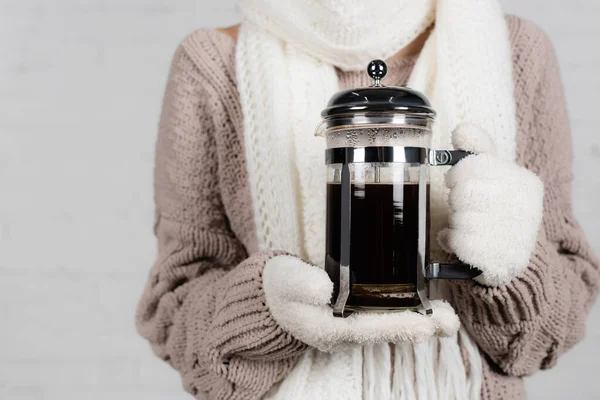 Cropped view of woman in knitted sweater and gloves holding coffee pot on white background — Stock Photo