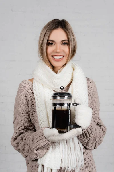 Femme souriante en écharpe tricotée et pull tenant une cafetière sur fond blanc — Photo de stock