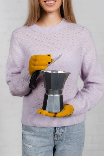 Vista recortada de la mujer sonriente en suéter caliente y guantes que sostienen la cafetera géiser sobre fondo blanco - foto de stock
