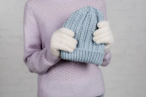 Cropped view of woman in warm sweater and gloves holding knitted hat on white background — Stock Photo