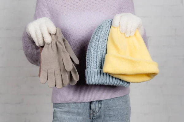 Cropped view of young woman holding soft gloves and hats on white background — Stock Photo