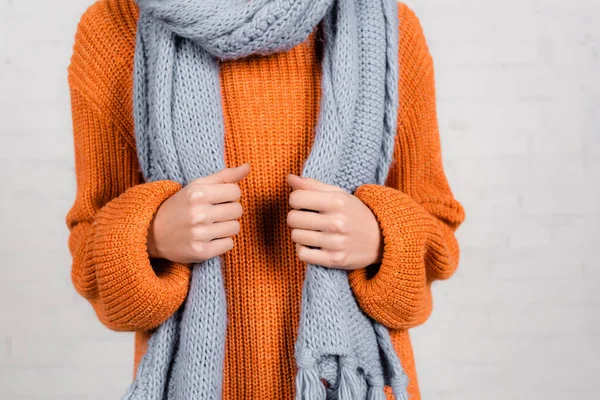 Cropped view of woman in orange knitted sweater and grey scarf on white background — Stock Photo